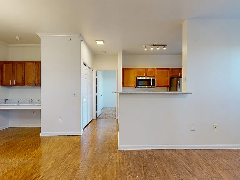 Apartment kitchen with stainless steel appliances, dining and living room with wood-style flooring and built-in desk.