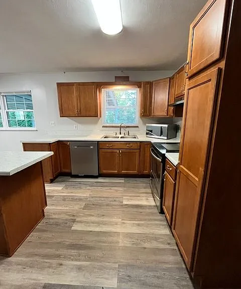 Updated kitchen featuring rich wood cabinetry, durable wood look LVP flooring, and generous counter space with a center island. The Kitchen includes stainless steel appliance, abundant cabinet storage, and a large window above the sink for natural light a