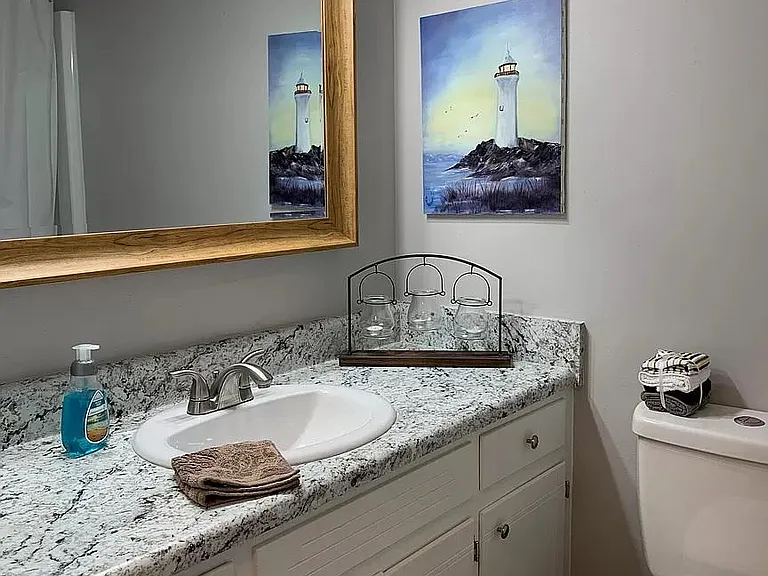 Hallway bathroom with lots of storage, framed mirror, large countertop and tub/shower combo