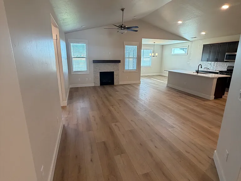 The spacious open-concept living area features a beautiful fireplace as its focal point, creating a warm and inviting atmosphere. Gorgeous wood flooring flows throughout the space, seamlessly connecting the living, dining, and kitchen areas.