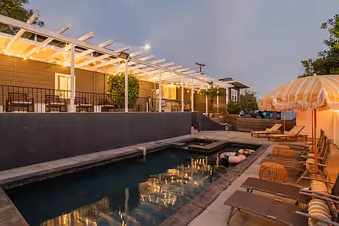 Resort-style outdoor space with a heated pool, hot tub, sun loungers with umbrellas, and cozy seating. Perfect for relaxing, sunbathing, or enjoying poolside drinks, this stylish area offers a luxurious retreat for ultimate leisure.