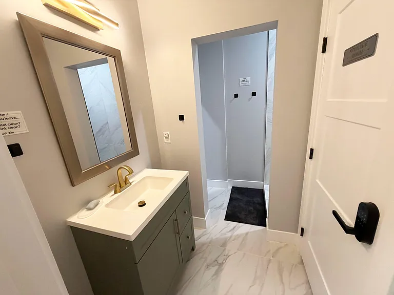Bathroom vanity area with a wide framed gold colored mirror, quartz-style counter, and tiled flooring leading to the shower