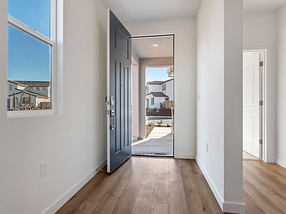 A bright and airy hallway with a wooden floor, leading to an open doorway that reveals a view of the