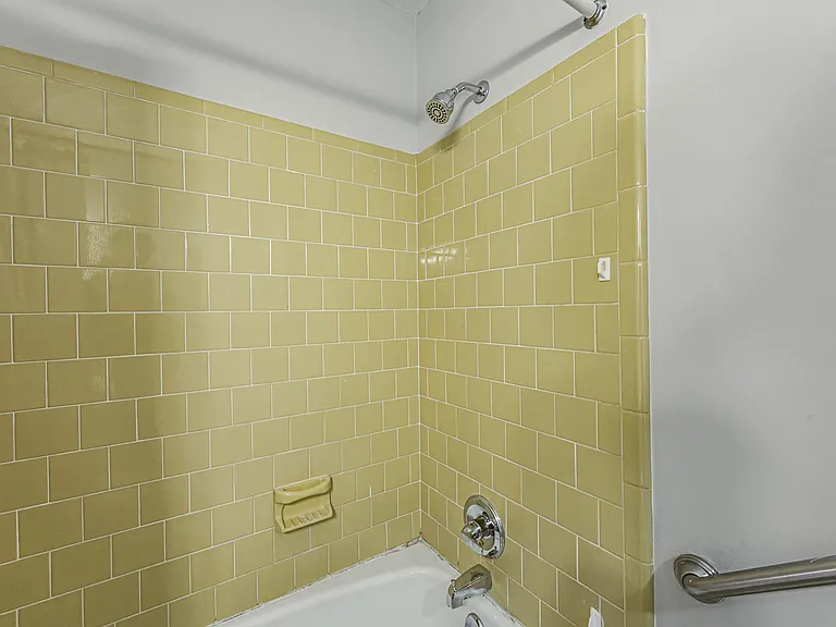 Tub/shower combo with tiled surround, built-in soap dish, and grab bar for added convenience and support.