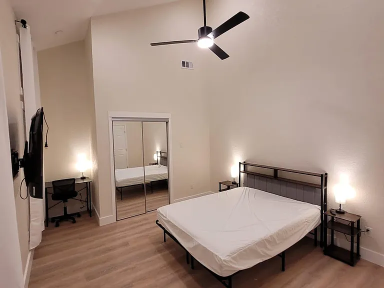 Spacious bedroom with high ceilings, ceiling fan, mirrored closet doors, and space for a desk plus bedside tables.