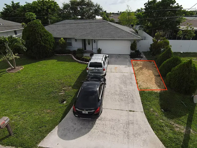 Single-story home with a wide driveway, attached garage, and a spacious front lawn with mature landscaping.