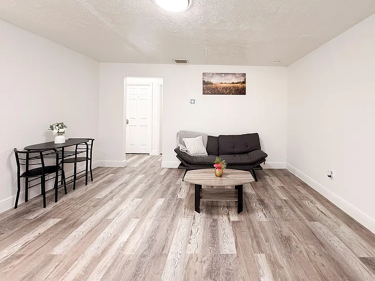 Open common living area with durable wood-look flooring, a lounge seating setup, and a small dining nook for daily meals.