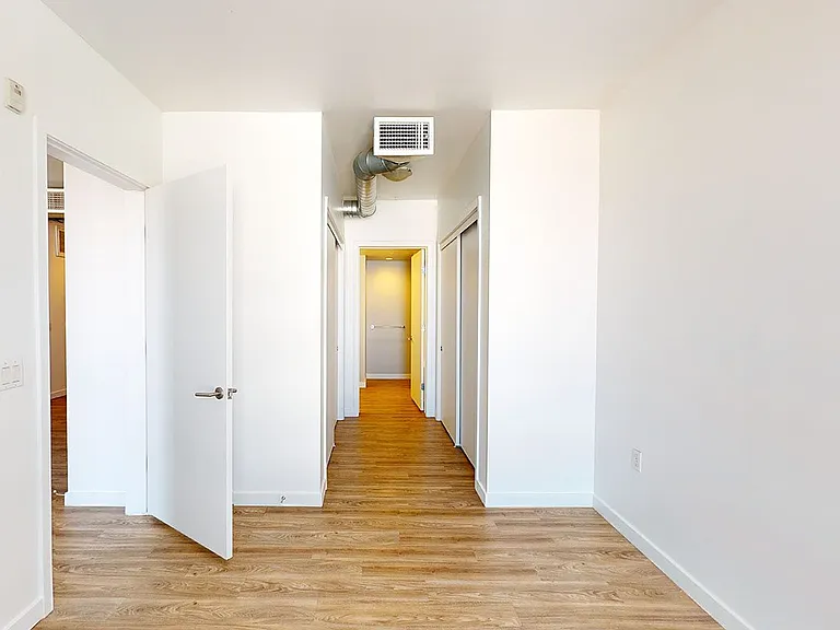 Spacious apartment bedroom with attached bathroom and wood-style flooring.