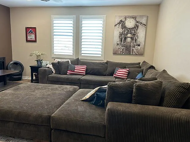 Spacious living room with a large sectional, side table, and two shuttered windows for natural light.