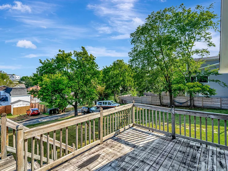 Elevated back deck with wood railings overlooking a fenced yard and mature treesideal for outdoor seating and relaxing.