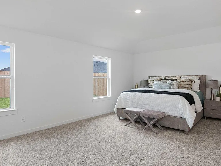 Spacious carpeted bedroom with two windows for natural light and ample wall space for storage and a desk setup.