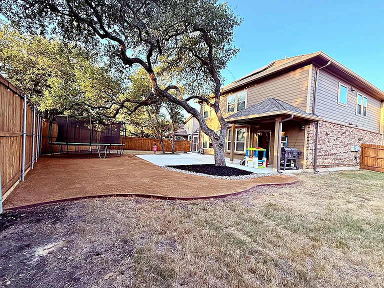 Spacious fenced backyard shaded by a mature oak, with patio and open play space.