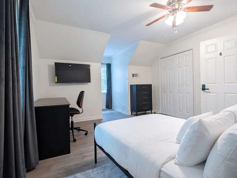 Furnished bedroom with a full bed, desk setup, and wall-mounted TV, plus a closet and ceiling fan for comfort.