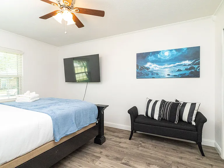 Bedroom 3 boasts a queen sized bed, cozy wood bed frame and headboard, a flat-screen Roku TV, and a comfy love seat_creating a peaceful and inviting space to relax and unwind. There is an attached closet with hangers and a luggage rack.