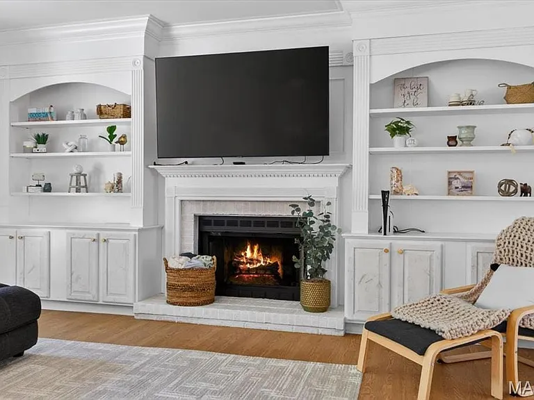 Central fireplace featuring a stone hearth and surround, flanked by custom built-in cabinetry with arched open shelving and lower storage