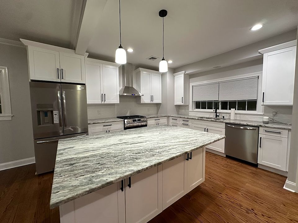 Designer kitchen with large granite island, new stainless-steel appliances, and modern black hardware.