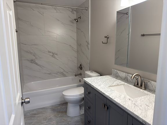 Modern fully remodeled bathroom featuring a sleek marble-look tile shower, updated vanity with stone countertop, and brushed nickel fixtures throughout.