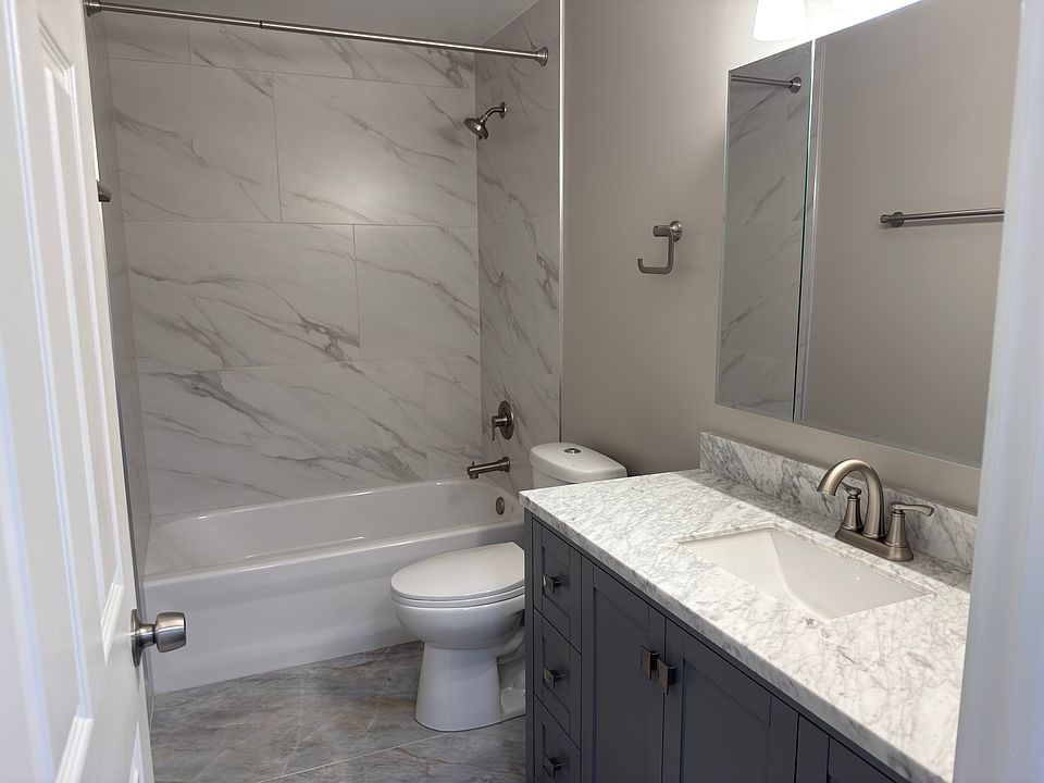 Modern fully remodeled bathroom featuring a sleek marble-look tile shower, updated vanity with stone countertop, and brushed nickel fixtures throughout.