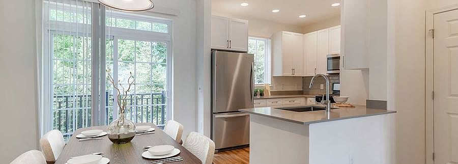 Newly renovated Finish Package III kitchen and dining area with white cabinetry, grey quartz countertops, hard surface flooring, stainless steel appliances, and tile backsplash