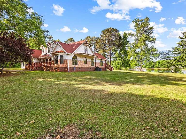 Spacious home set on a large, grassy lot with mature trees, a wraparound deck, and scenic water views nearby.
