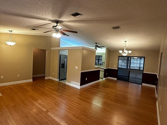 Open-concept living and dining space with natural light, wood floors, ceiling fans, and elegant lights.