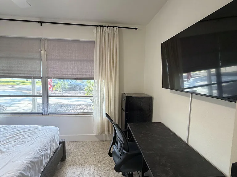 Private bedroom with a large window, ceiling fan, and a dedicated work desk plus wall-mounted TV for easy living.
