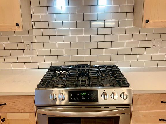 Stainless steel vent hood over stove and oven in between custom wood cabinets with tile backsplash.