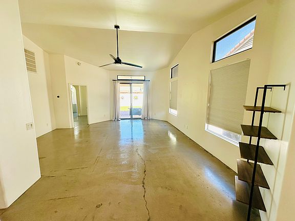 Large living room, modern concrete floors, high ceiling, large windows and large sliding glass door to backyard.