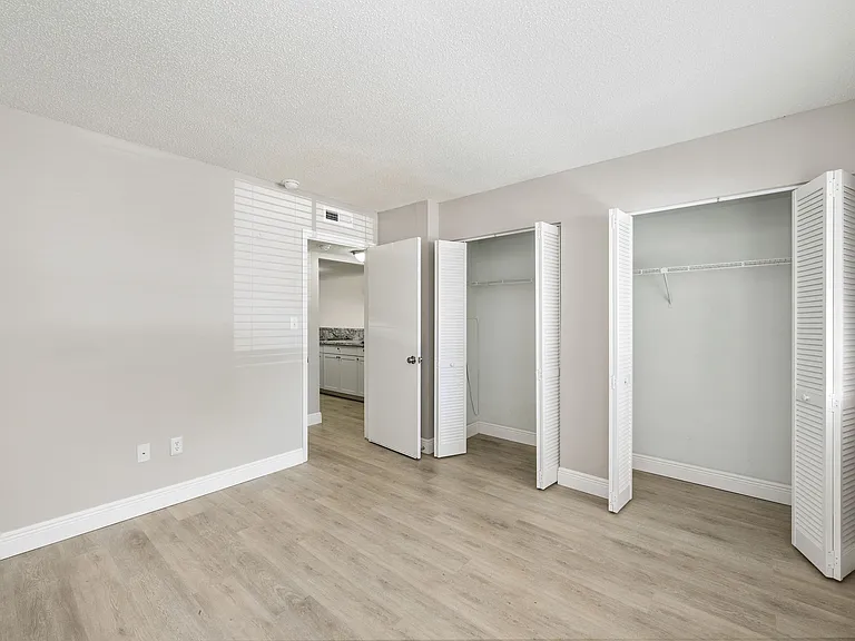 Bright, spacious bedroom with sleek hardwood flooring, ample closet space, and natural light filtering through large windows.