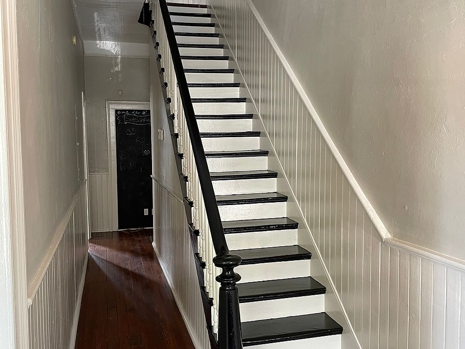 Downstairs hallway freshly painted pale grey with white wainscoting. Stairway painted with black and white stair treads and risers