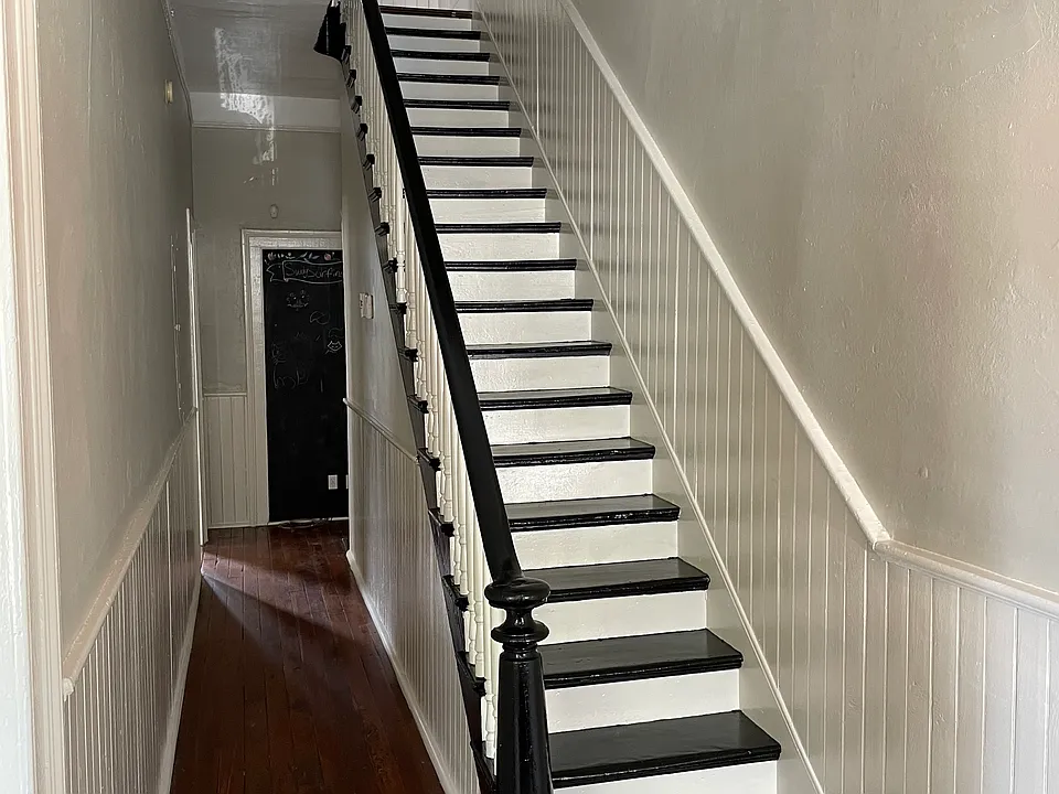 Downstairs hallway freshly painted pale grey with white wainscoting. Stairway painted with black and white stair treads and risers