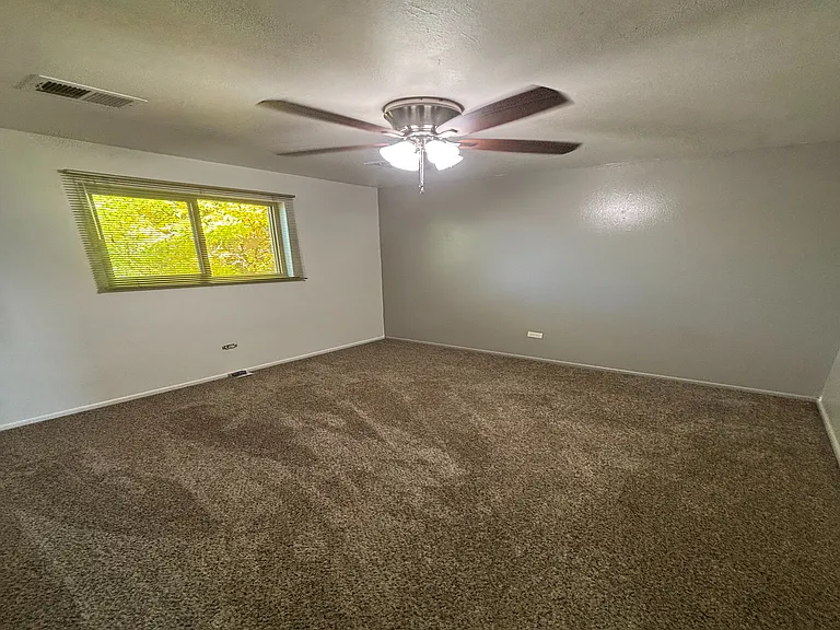 Cozy bedroom with soft carpet flooring, ceiling fan, and abundant natural light from a large window.