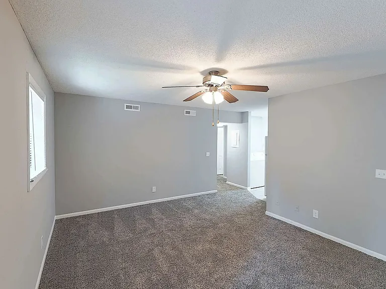 Spacious bedroom with plush carpeting, ceiling fan, and natural light