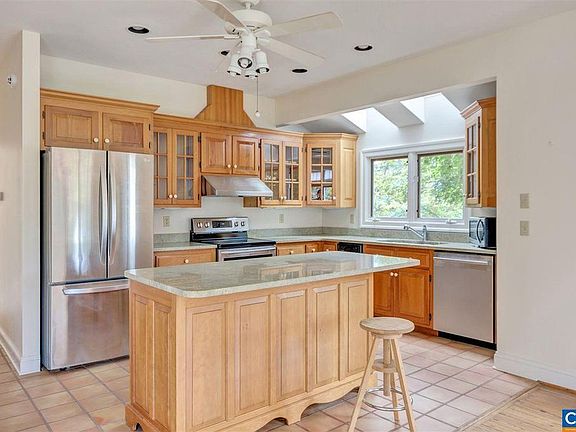 The kitchen has custom cabinetry and sea green granite countertops. There are two skylights at the stainless steel sink. The oven/stove is electric. The floor is terra cotta tile.