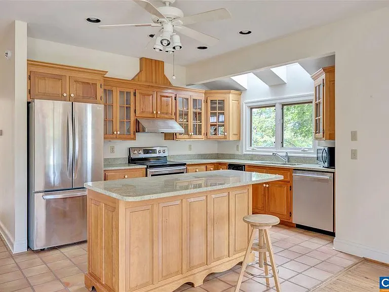 The kitchen has custom cabinetry and sea green granite countertops. There are two skylights at the stainless steel sink. The oven/stove is electric. The floor is terra cotta tile.