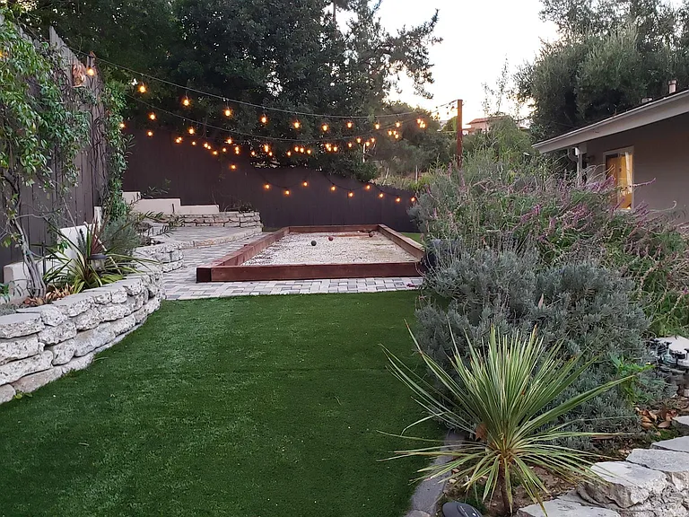 Backyard with Bocce Court and low maintenance landscaping with artificial grass and live plants peppered in.