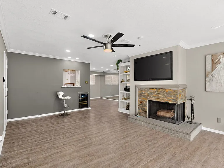 Bright living room with a fireplace and a ceiling fan, adjacent to a dry bar; perfect for relaxation.