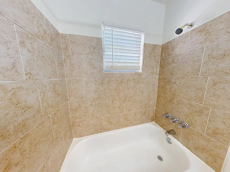 Bright bathroom featuring elegant beige tile walls, a clean white bathtub, and a modern shower fixture, perfect for relaxation.