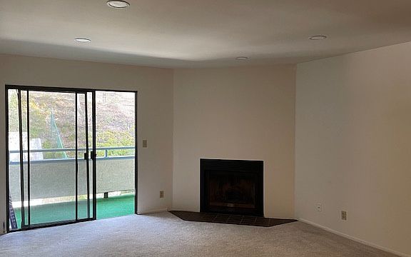 Bright and open living room featuring a cozy fireplace and sliding glass doors leading to a private balcony with hillside views.