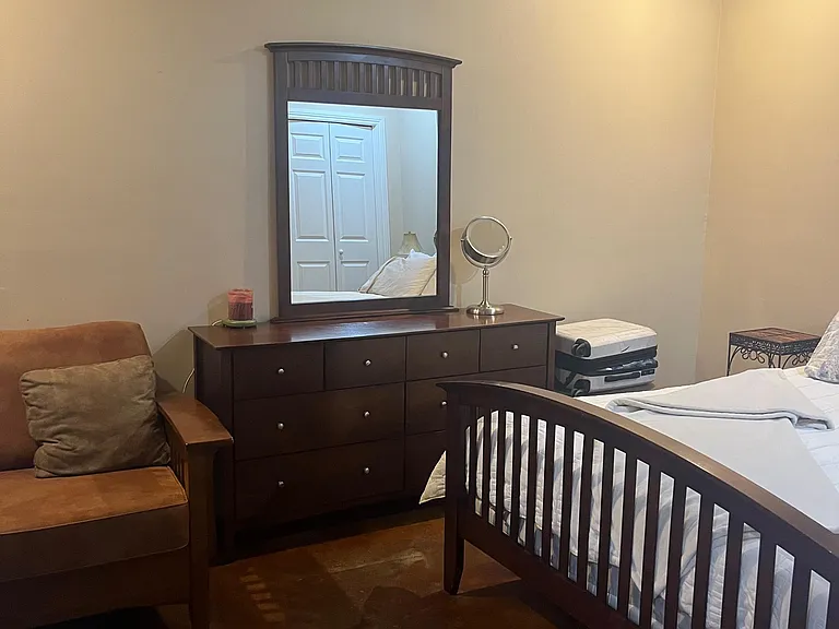 Furnished bedroom with a full bed, dresser with mirror, and sitting chair, offering practical comfort and storage.