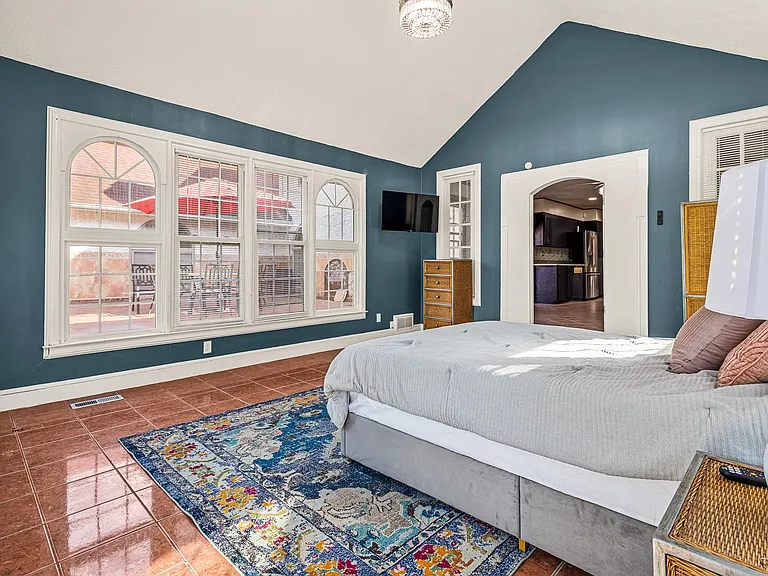 Spacious bedroom with large arched windows, tile flooring, and a mounted TV, plus easy access to the main living areas.