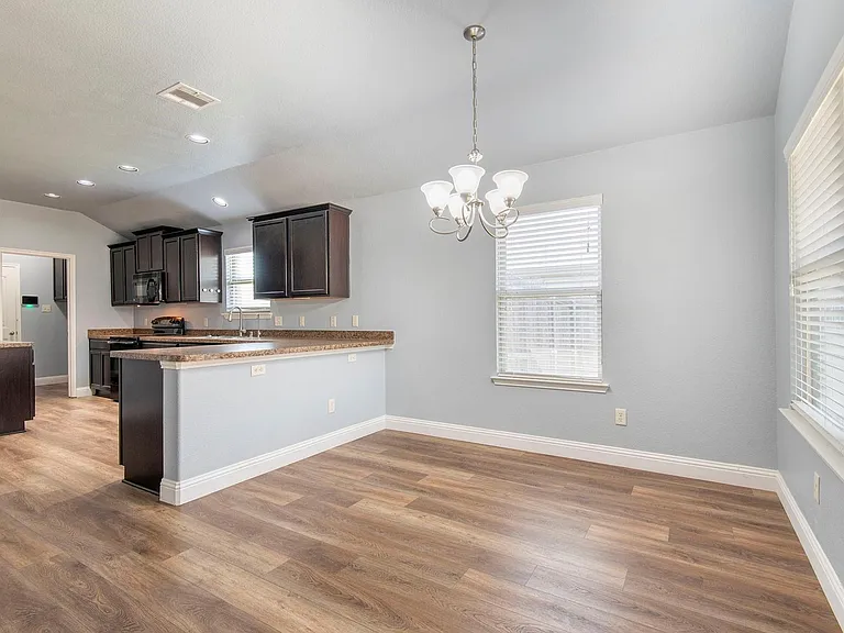 Kitchen with a chandelier, a peninsula, pendant lighting, dark wood finished floors, and lofted ceiling