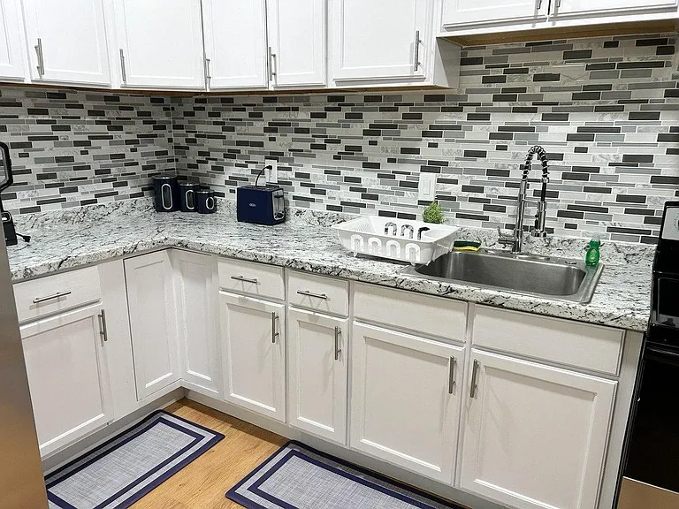 Updated kitchen with white cabinetry, granite-look counters, mosaic tile backsplash, and a deep stainless sink for easy meal