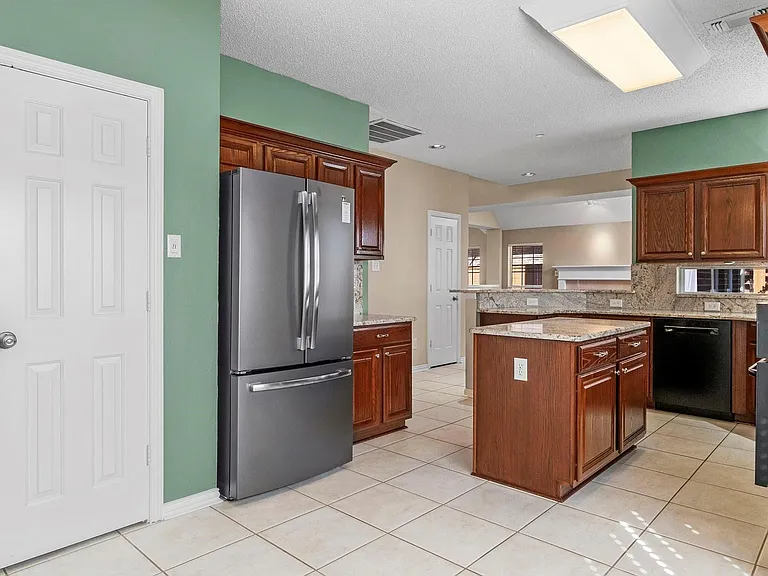 Kitchen featuring a central island, rich wood cabinetry, light tile flooring, and integrated stainless steel appliances