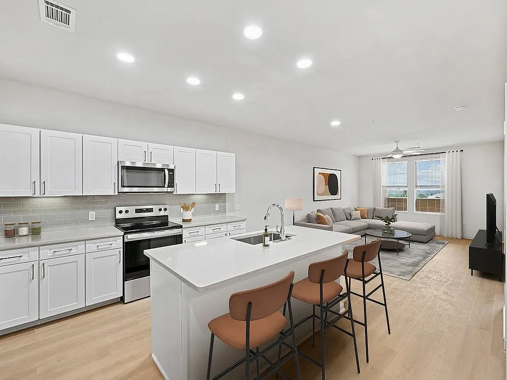 Renovated Package I kitchen with white cabinetry, grey quartz countertops, grey subway tile backsplash, stainless steel appliances, and hard surface flooring - Avalon Denver West