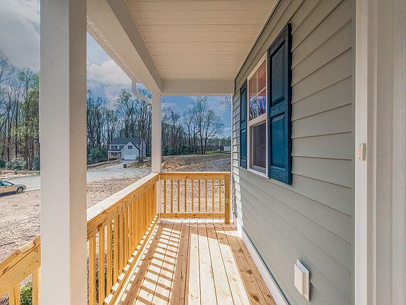 A wooden porch with railings attached to a light gray house with blue window shutters. The area is u