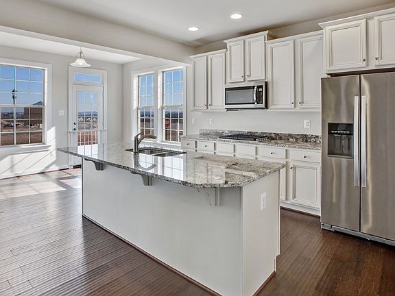 White open kitchen with large island with sink, stainless steel appliances and recessed lights.