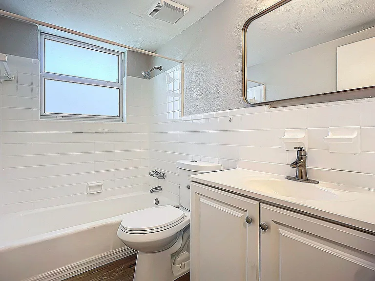 Bright and modern bathroom featuring a sleek white vanity, spacious bathtub, and elegant fixtures, filled with natural light from a large window.