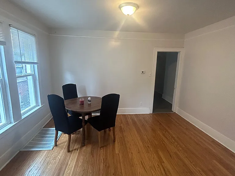 Dining area with hardwood floors, overhead lighting, and a window with blinds, offering space for a small table setup.