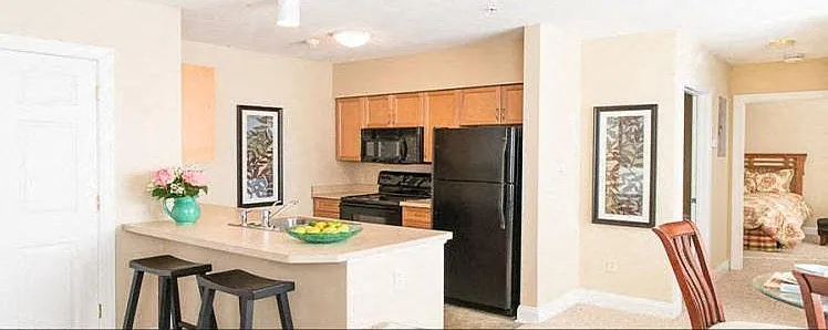 Well equipped ktichen with breakfast bar, black appliances, and view down hallway towards bedroom